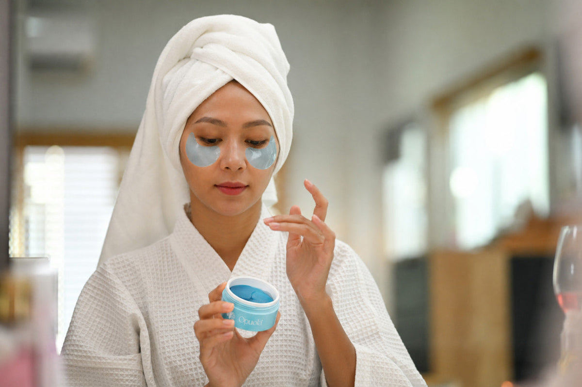 Woman wearing blue hydrogel under-eye patches in the morning, holding an open jar of Opuola Aloha Blue Patches