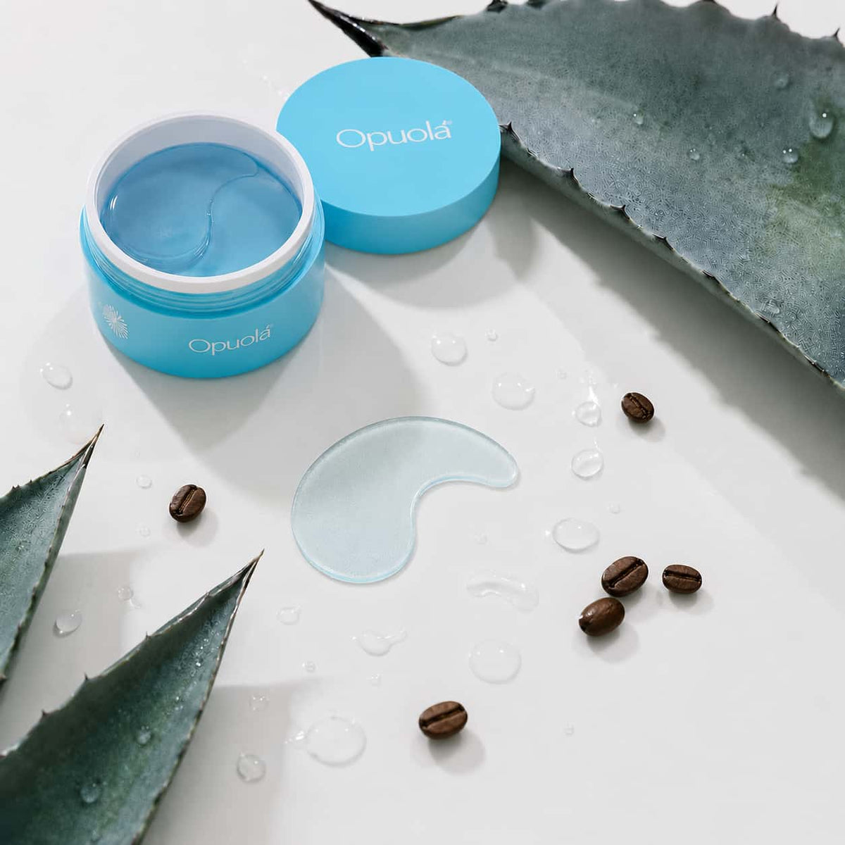 Aloha Blue Patches hydrogel under-eye patches with blue agave, coffee beans and serum droplets showing the depuffing ingredients, Opuola.