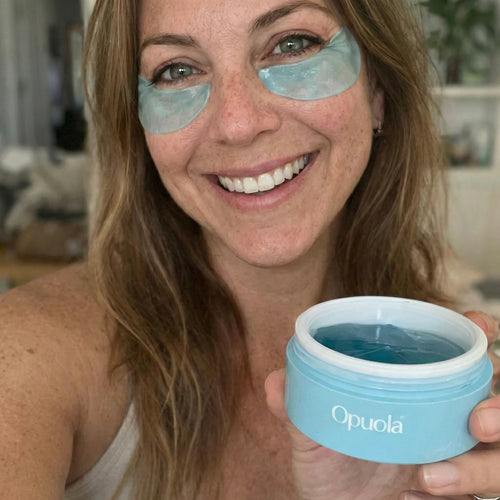 Woman in her 40s wearing Opuola Aloha Blue hydrogel under-eye patches, holding the blue jar — real customer result
