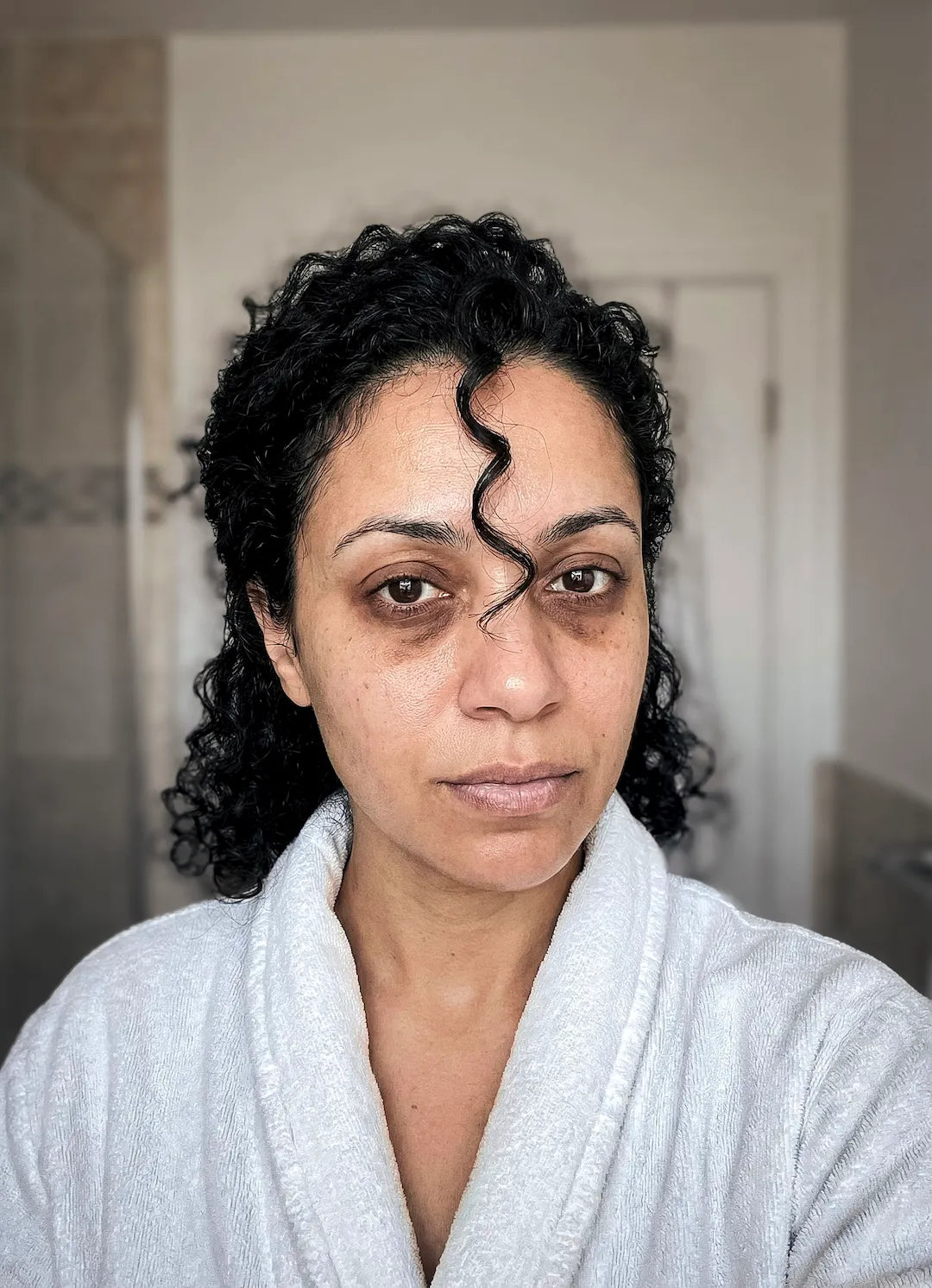 40-year-old mixed-race woman with pronounced under-eye dark circles and natural skin texture looking at herself in the morning