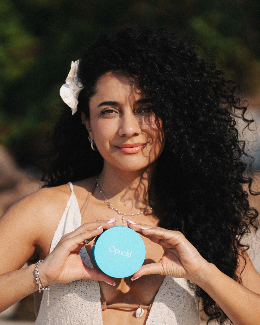 Woman holding Opuola Blue Agave under-eye patches in natural sunlight, showcasing radiant and refreshed skin
