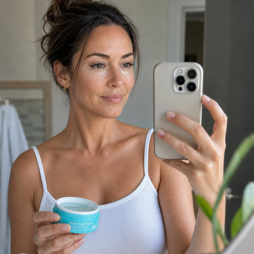 Woman taking a mirror selfie while holding an open jar of Aloha Blue hydrogel under-eye patches, Opuola